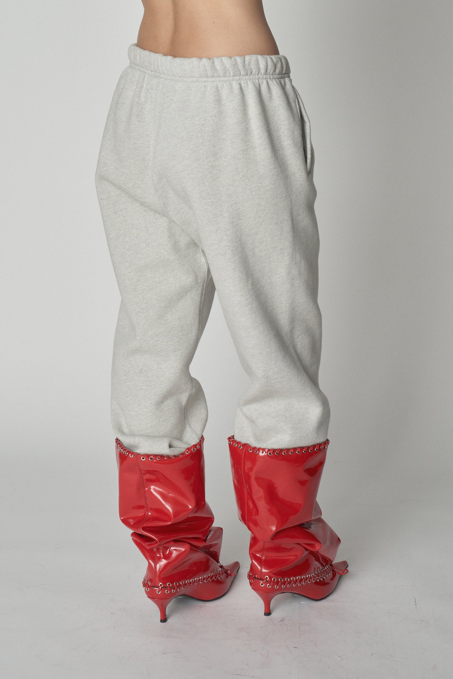 Waist down view of grey sweatpants with red boots.