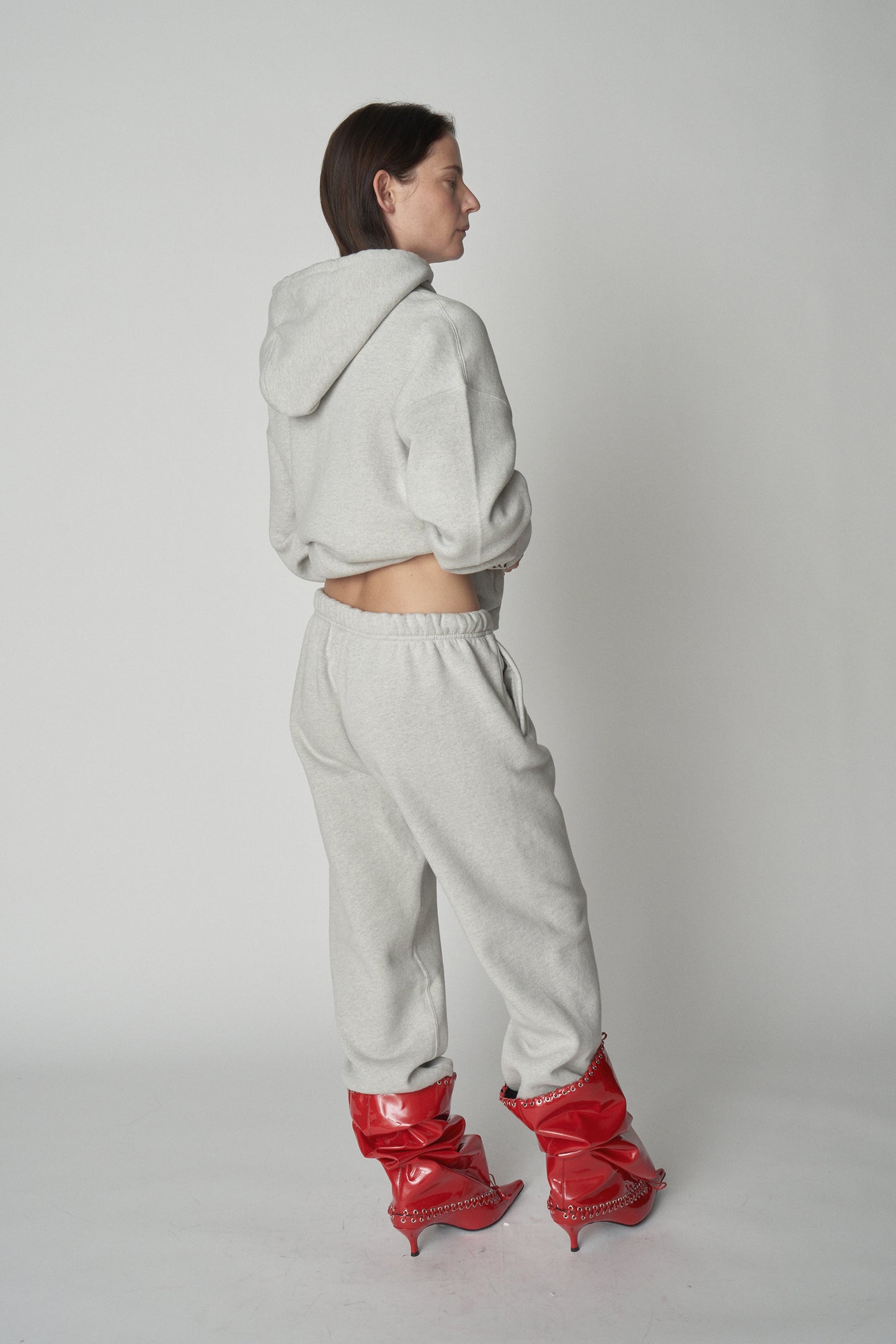 Full length back view of model wearing grey Absolutely Fabrics hoodie and sweatpants with red heeled boot.