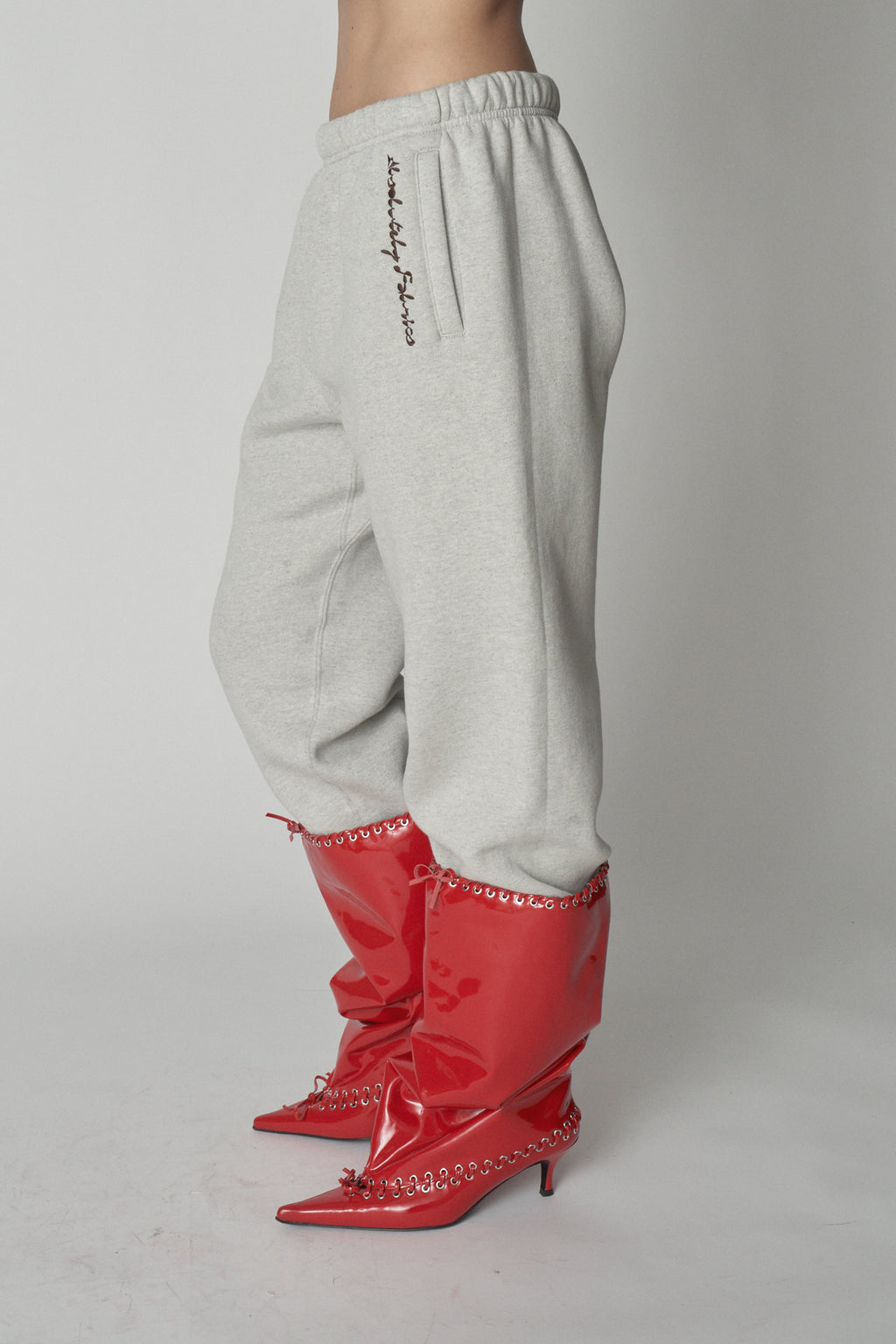 Waist down view of grey sweatpants with red boots.
