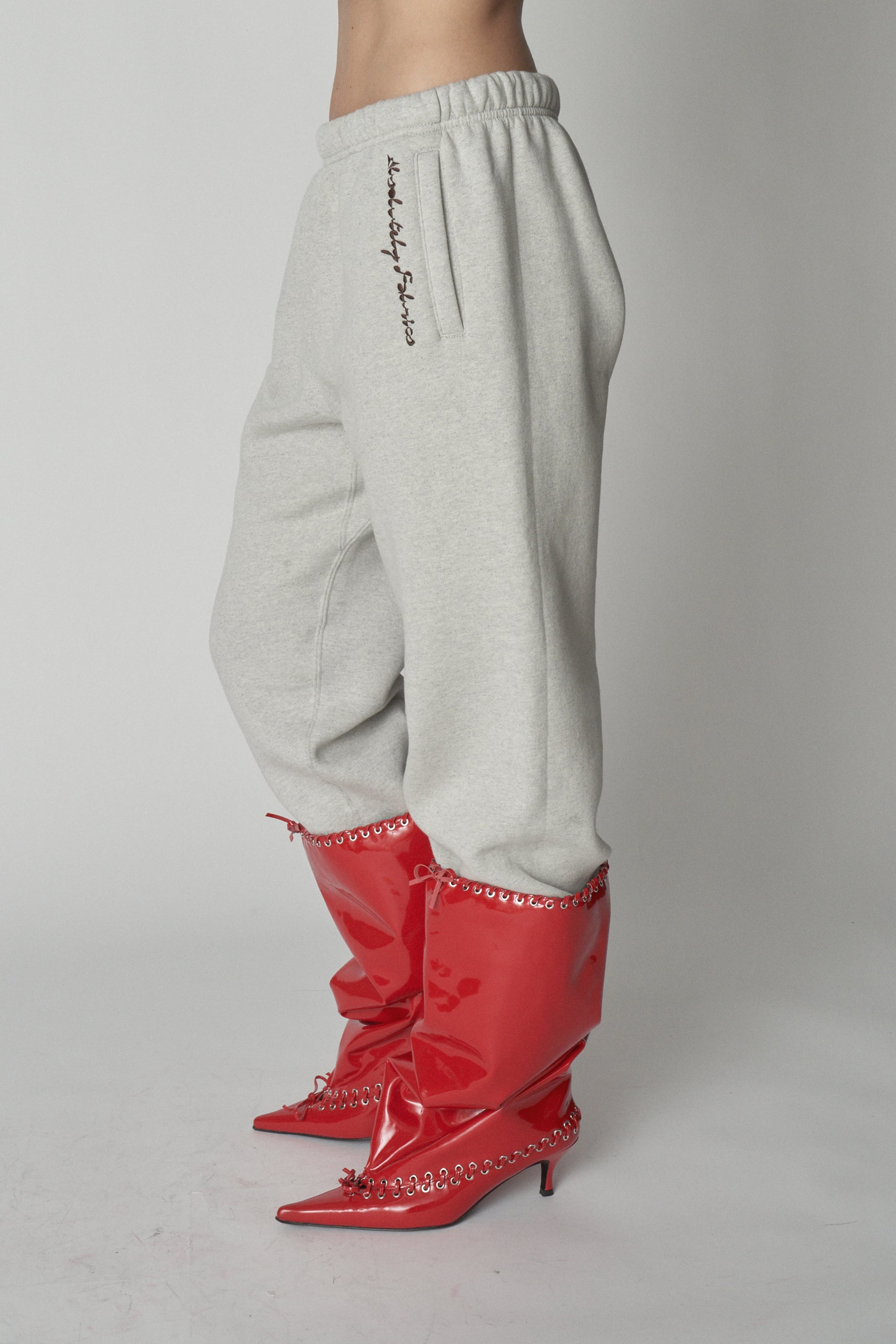 Waist down view of grey sweatpants with red boots.