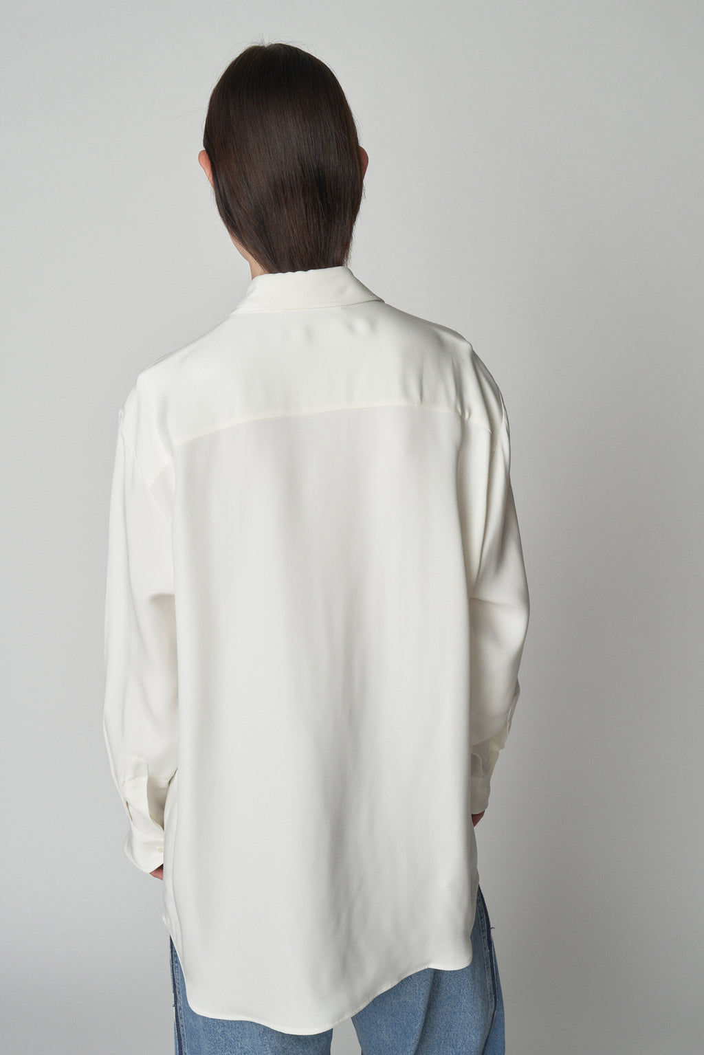Back torso view of model wearing relaxed white shirt. 