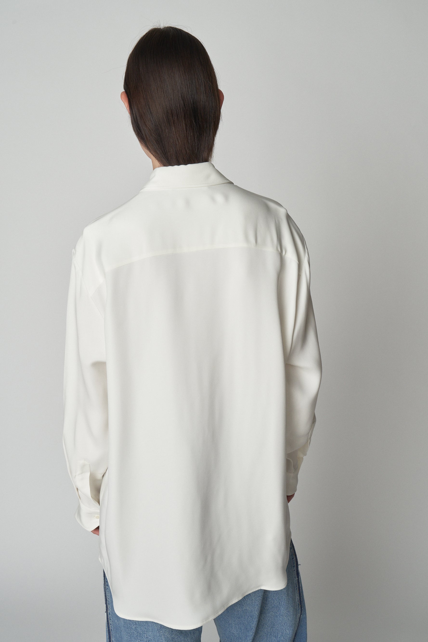 Back torso view of model wearing relaxed white shirt. 