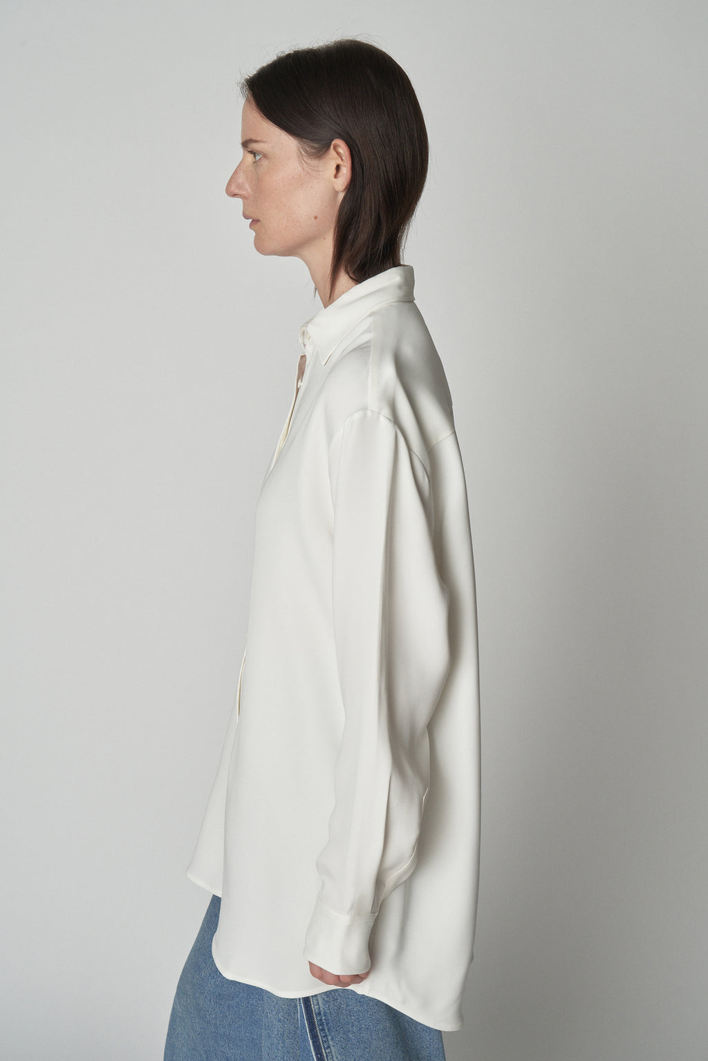 Side torso view of model wearing relaxed white shirt. 