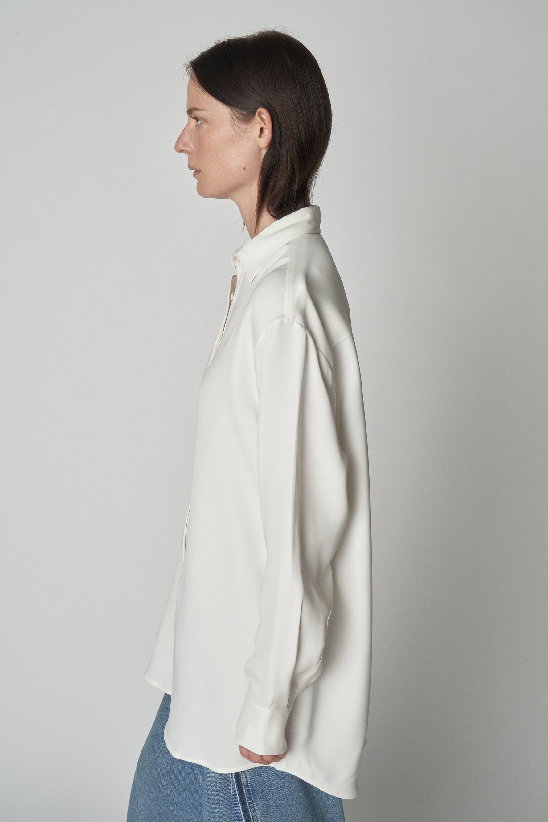 Side torso view of model wearing relaxed white shirt. 