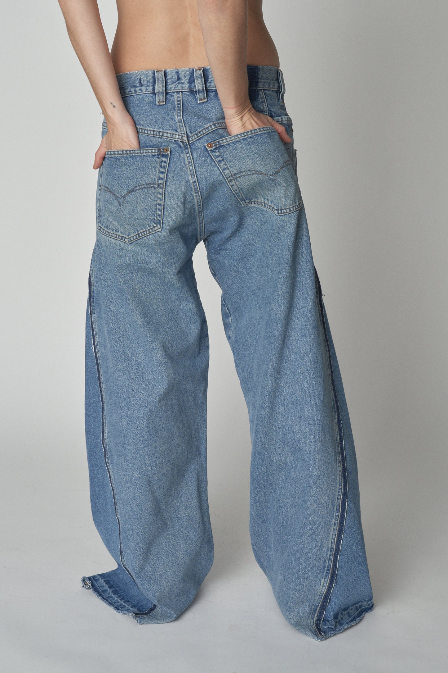 Back view of model wearing wide leg jeans with additional denim panel.