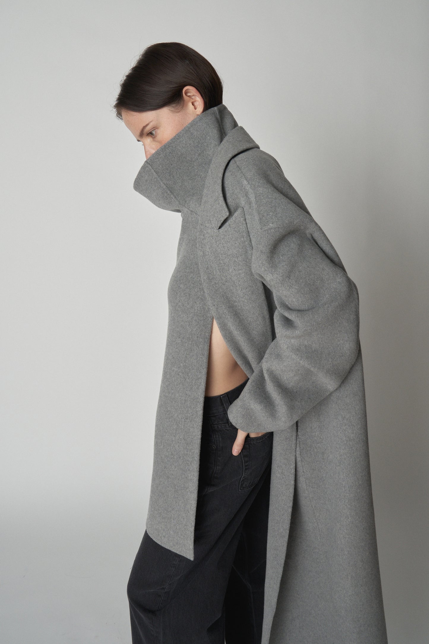 Side view of model wearing grey wool gilllet layered under matching trench coat. 