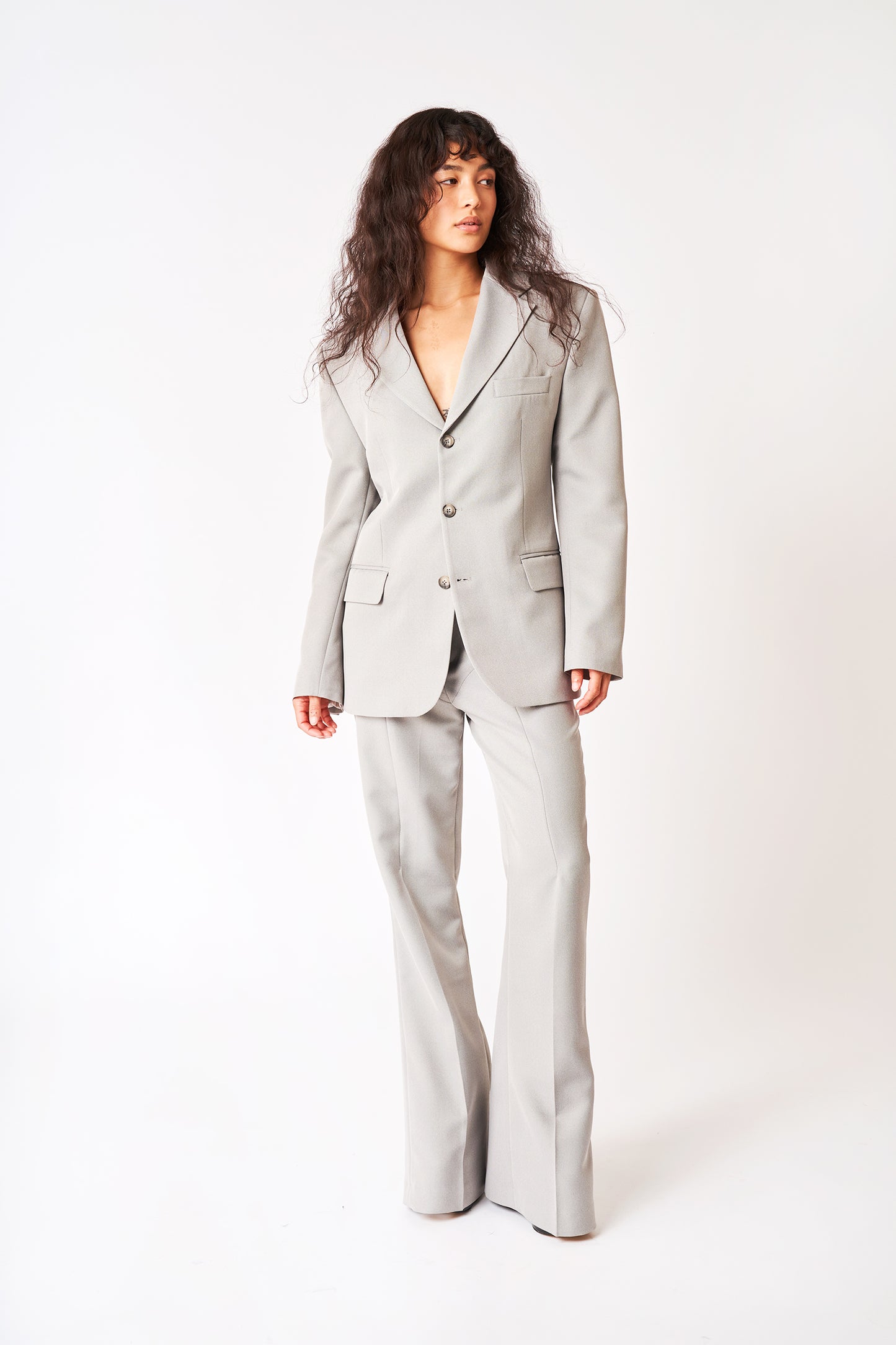 Model facing camera in Bettter grey suit with strong shoulder and flare trouser. 