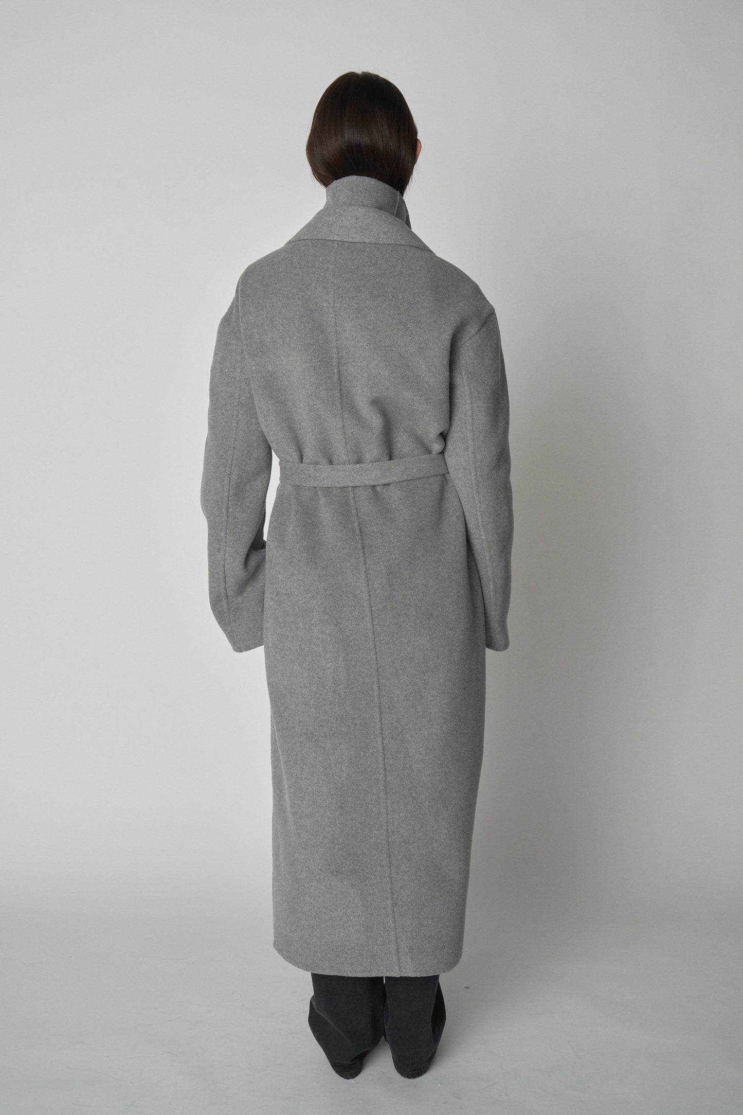 Back view of wearing grey trench-style wool coat. 