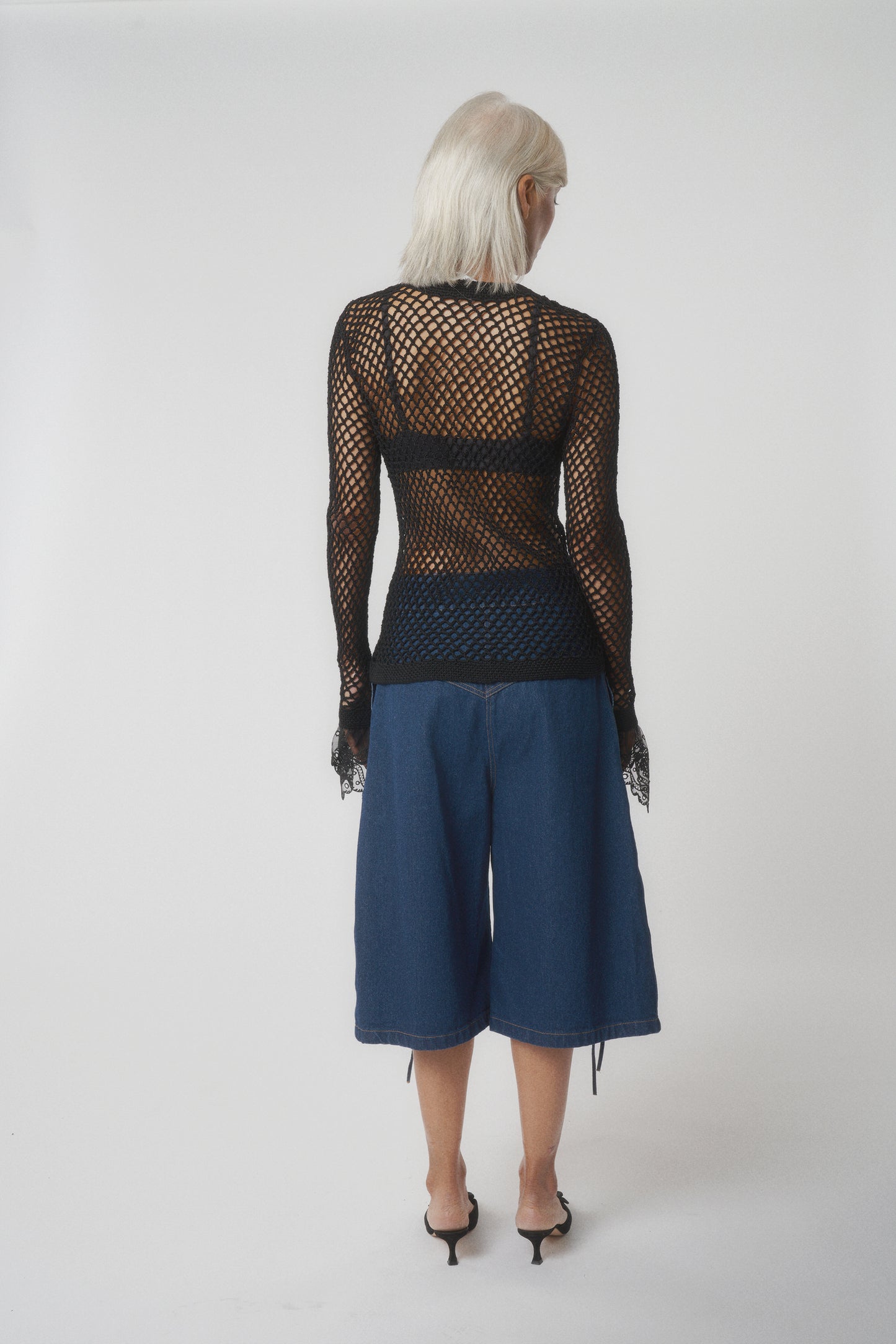 Back view of model wearing black net cardigan with white buttons and black lace sleeves.